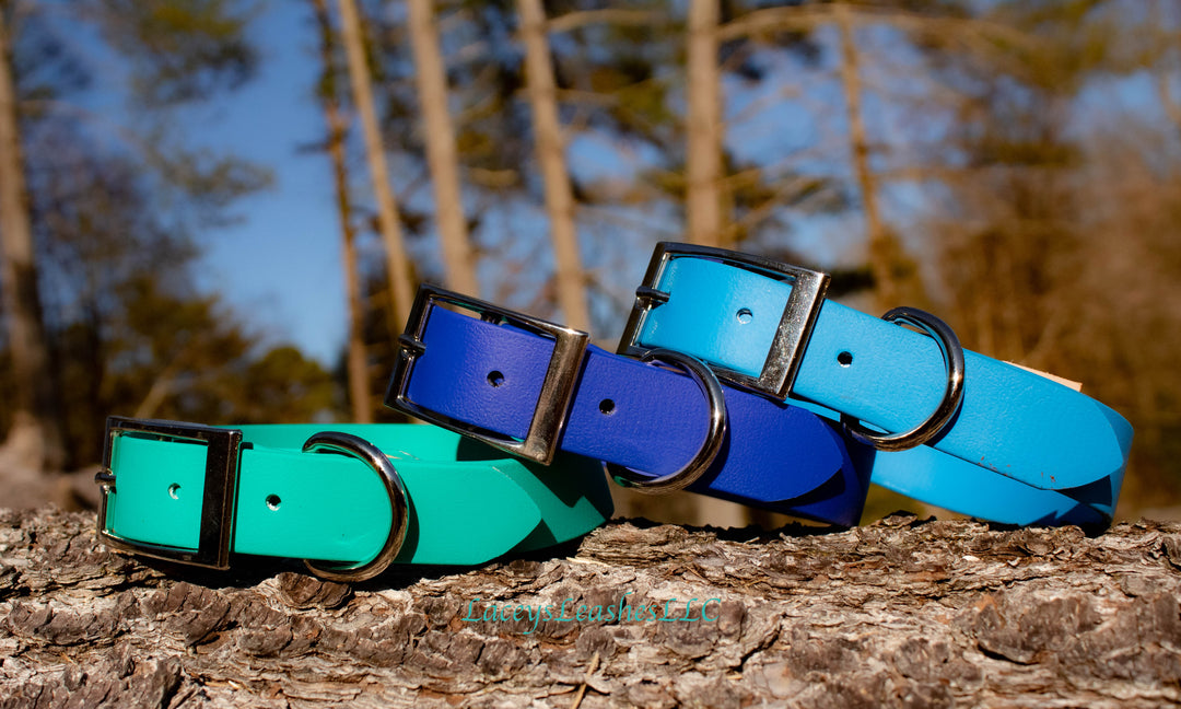 three different colored blue belt buckle collars sitting on a log.